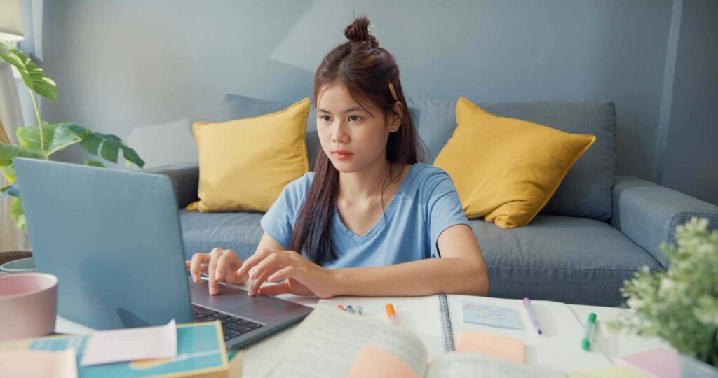 a young asian woman working on her laptop at home.