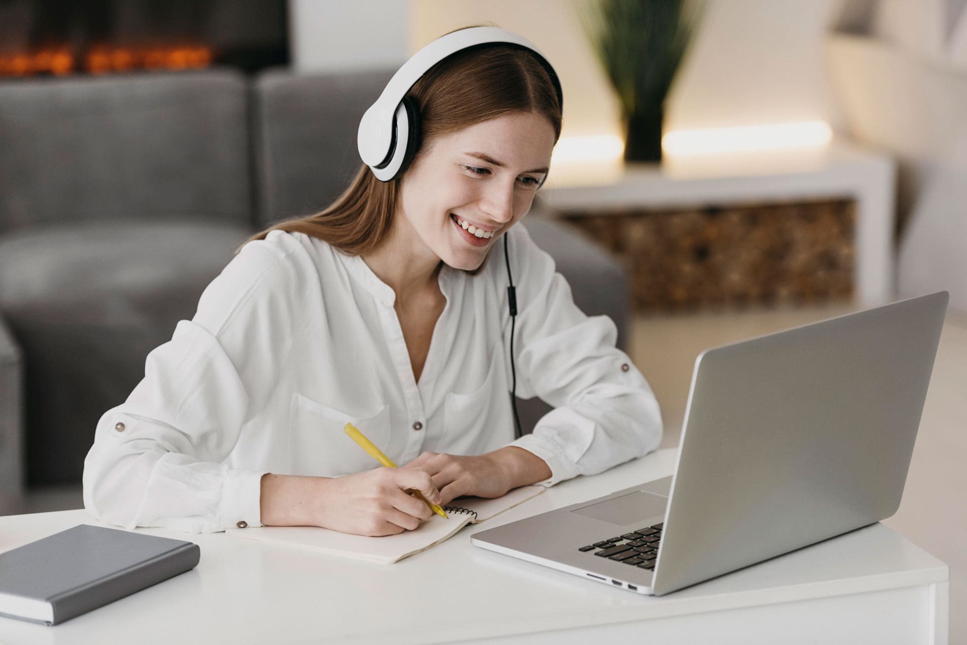 a woman wearing headphones and working on a laptop at home.